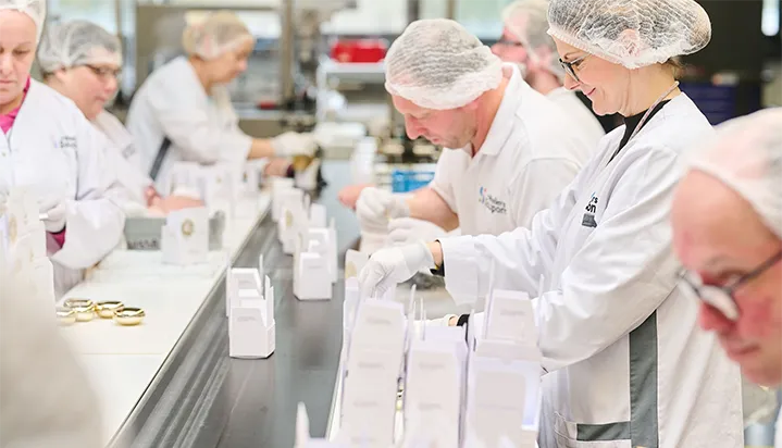 CONAPLUX_atouts Des personnes portant des charlottes et des blouses blanches travaillent à une chaîne d'emballage de produits blancs sur une table industrielle.