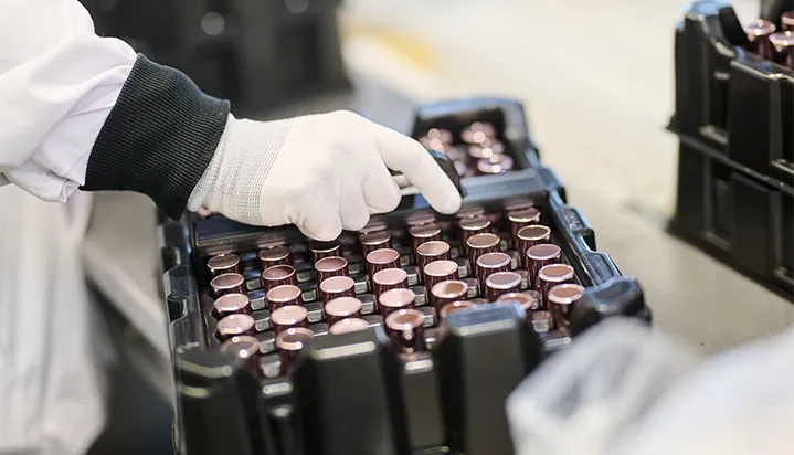 CONPALUX-conditionnement Une main gantée manipule des flacons métalliques alignés dans un plateau noir sur une surface industrielle.